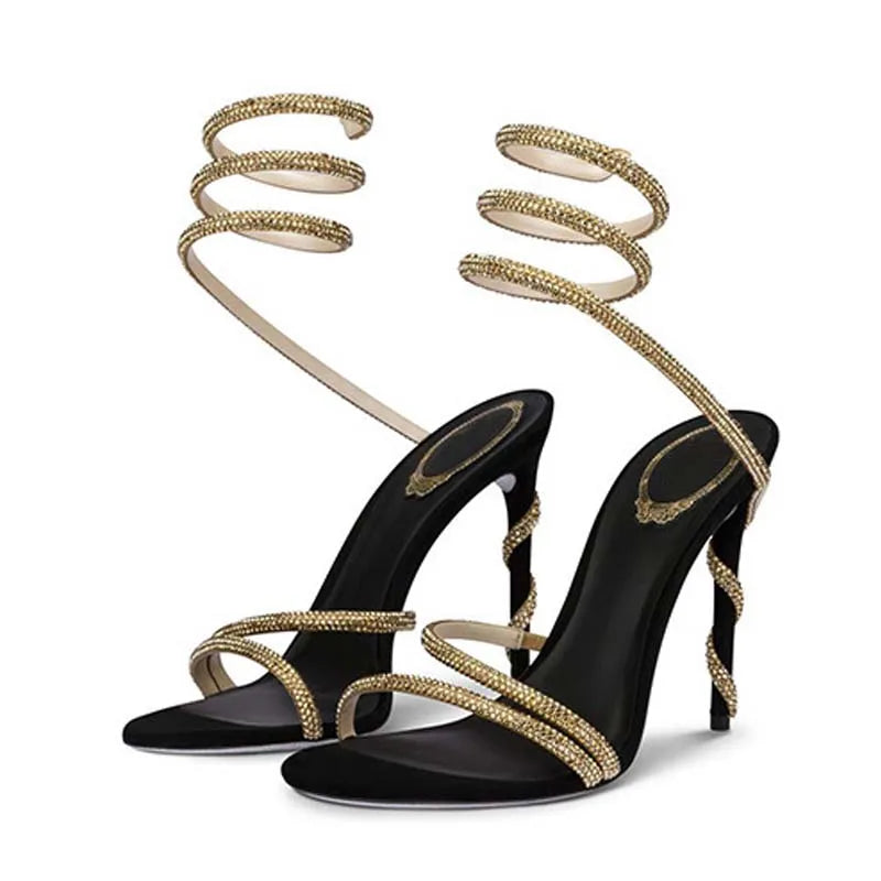 Black high-heeled sandals with gold spiral straps on a white background